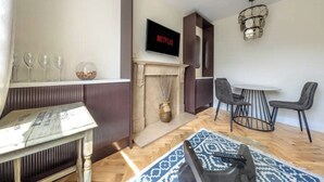 A modern living room with a fireplace, a dining area with a round table and chairs, and a television mounted on the wall displaying 'NETFLIX'.
