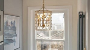 A modern interior with a geometric chandelier, a framed abstract painting, and a view of a brick building through a window.