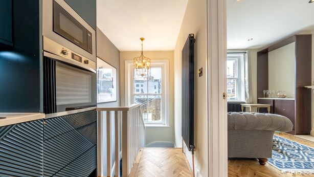 A modern kitchen with built-in appliances, a wooden herringbone floor, and a view to the outside.