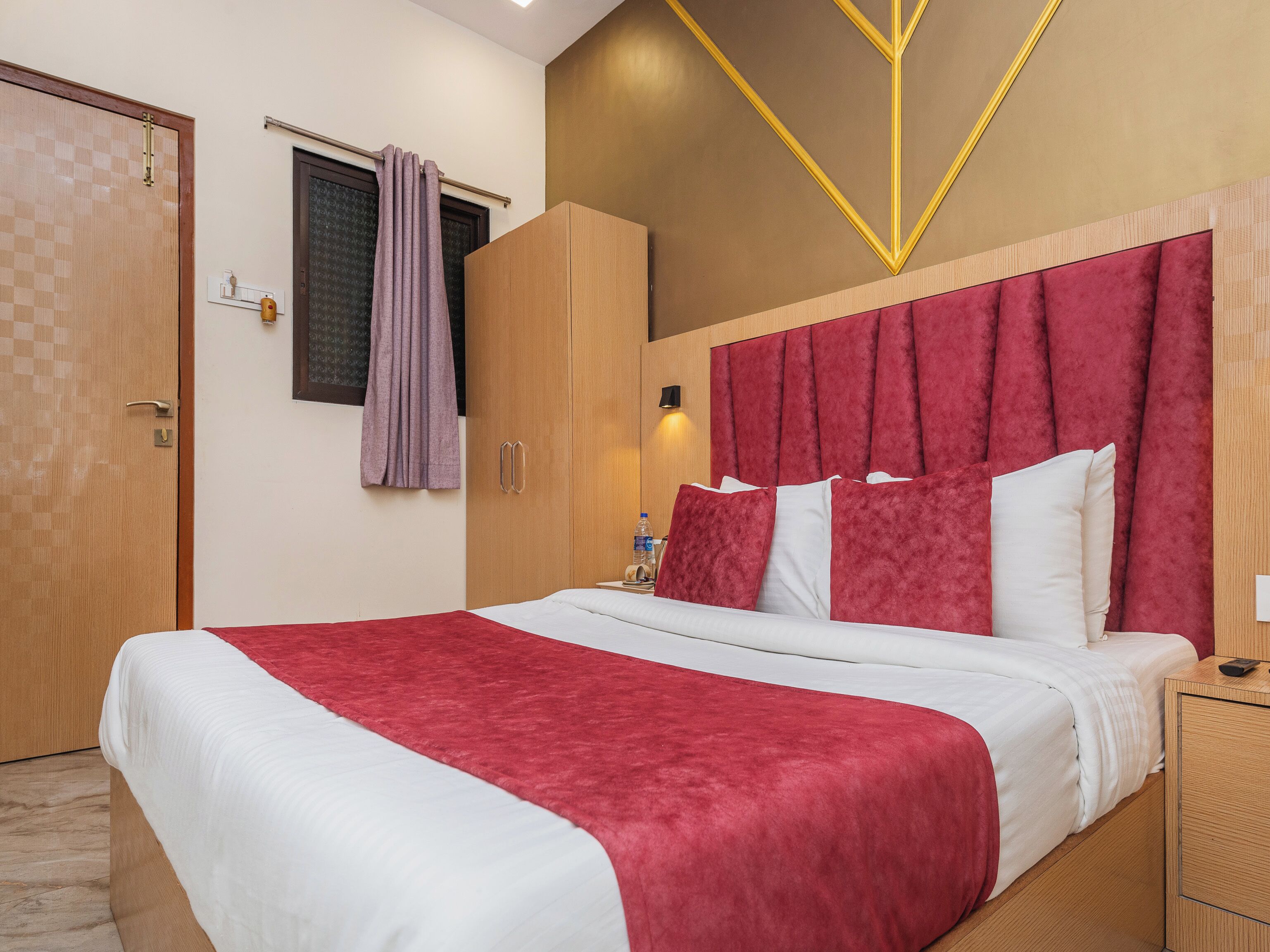 A hotel room with a large bed, wooden wardrobe, and a red headboard.