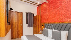 A hotel room with a bed, a wooden wardrobe, a ceiling fan, and a red patterned wall. - Hotel Priceless Suite (Mumbai)