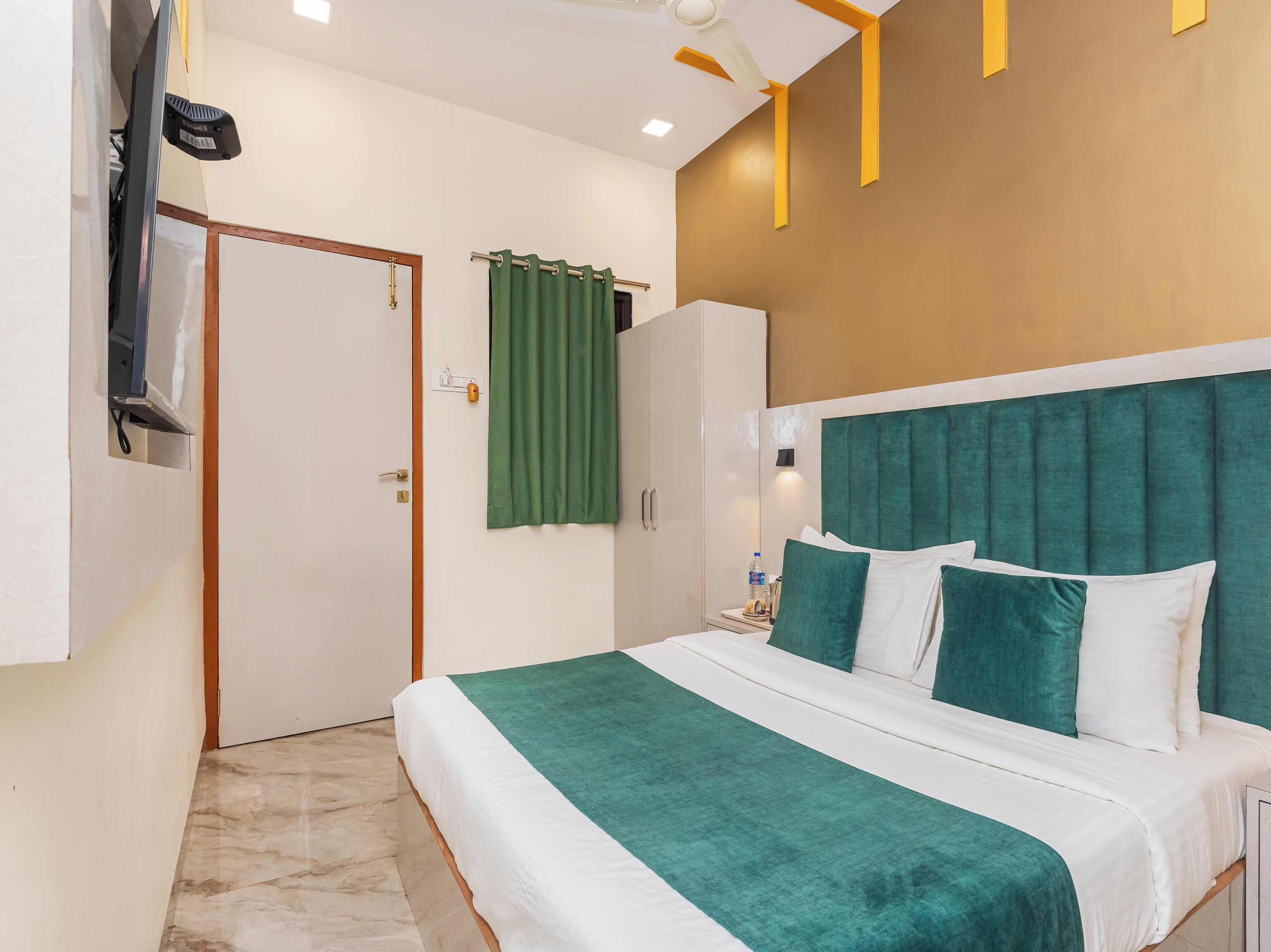 A hotel room with a bed, a wardrobe, a green curtain, and a ceiling fan.