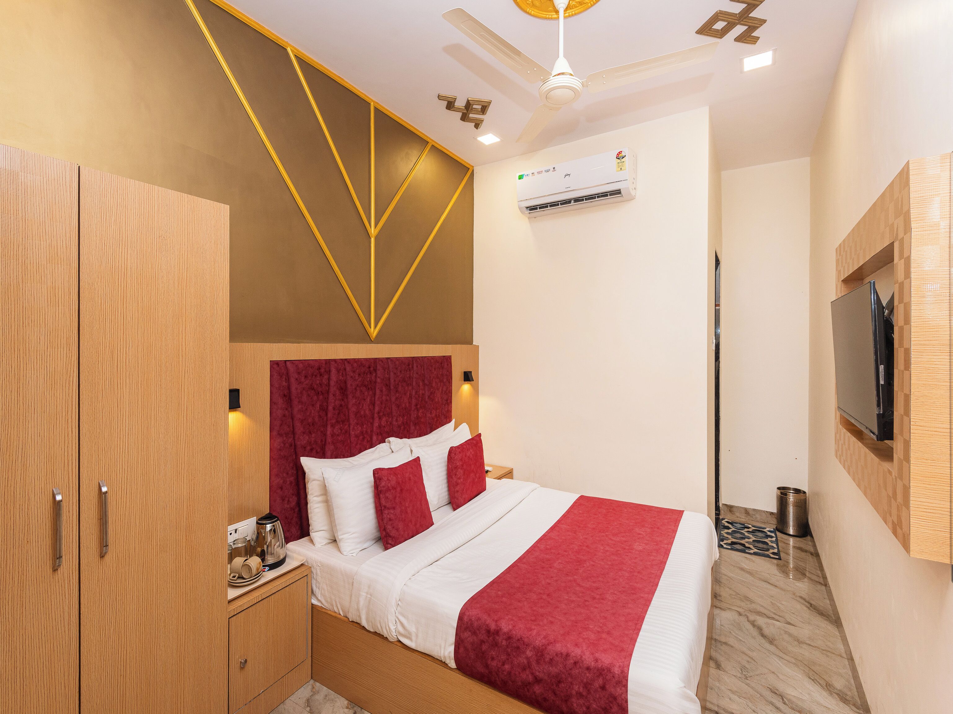 A hotel room with a bed, wardrobe, ceiling fan, air conditioning unit, and a mounted television.