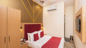 A hotel room with a bed, wardrobe, ceiling fan, air conditioning unit, and a mounted television.