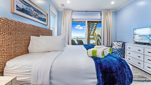 Een hotelkamer met een groot bed, een televisie, een rieten hoofdbord en uitzicht op de oceaan.