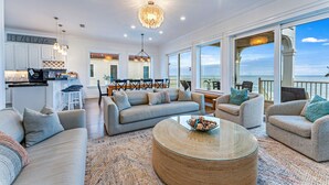 Een ruime woonkamer met een grote bank, een ronde salontafel en uitzicht op de oceaan.