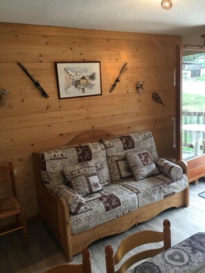 A cozy wooden room with a patterned sofa, a framed picture, and mounted knives on the wall. - Wifi, 2nd floor, parking, tv, ski locker, 26m², Arêches-Beaufort (Beaufort)