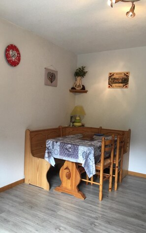 Un coin repas avec une table et des chaises en bois, une horloge, un tableau encadré et une petite étagère avec une plante.
