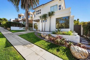 Uma casa moderna de dois andares com um jardim bem cuidado, um caminho pavimentado e uma grande formação rochosa.