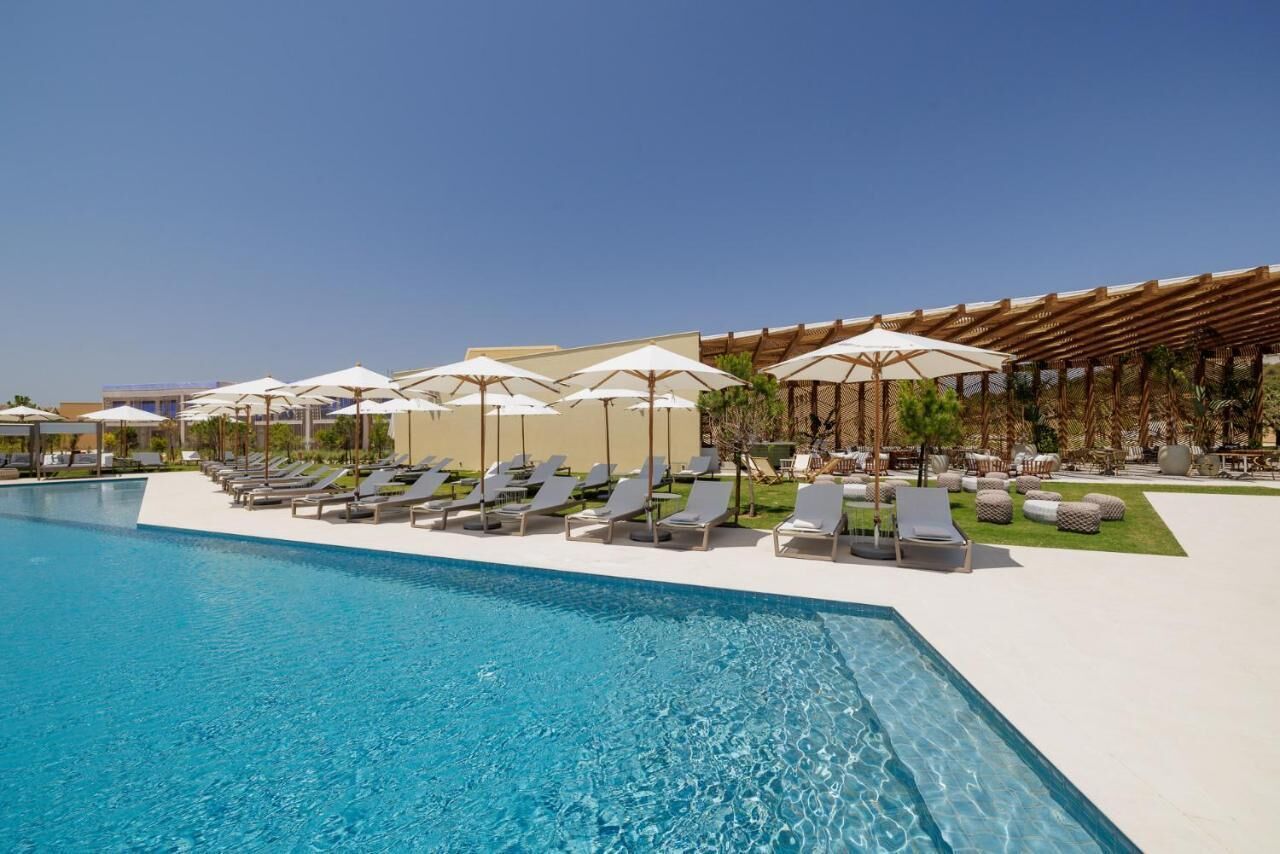 A poolside area with sun loungers and umbrellas, a clear blue pool, and a covered seating area.