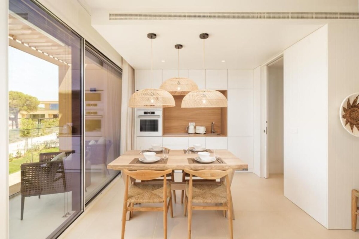 Une cuisine moderne avec une table et des chaises en bois, des luminaires suspendus et une vue à travers une porte vitrée.