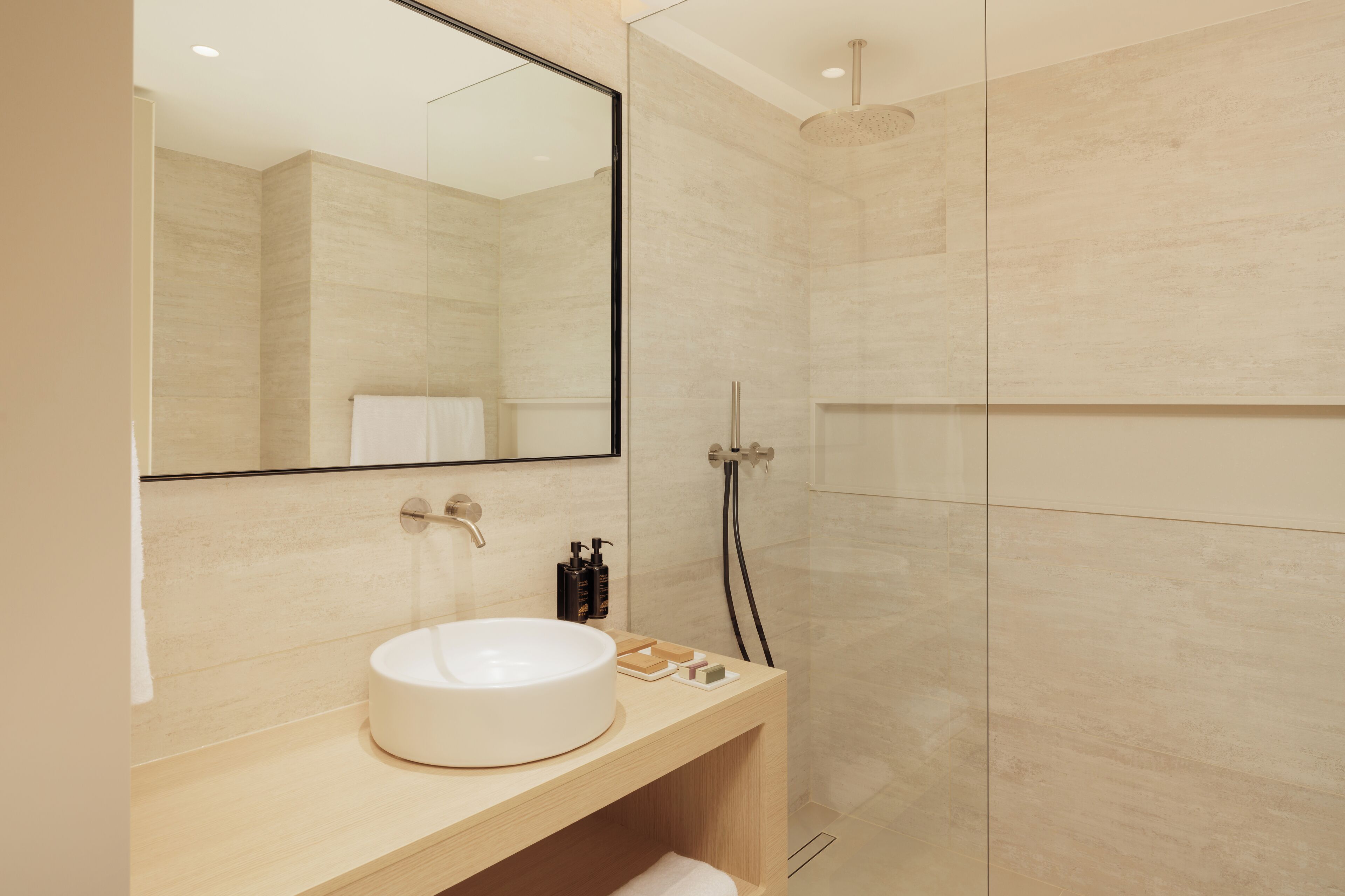 A modern bathroom with a large mirror, a round sink, and a shower area.