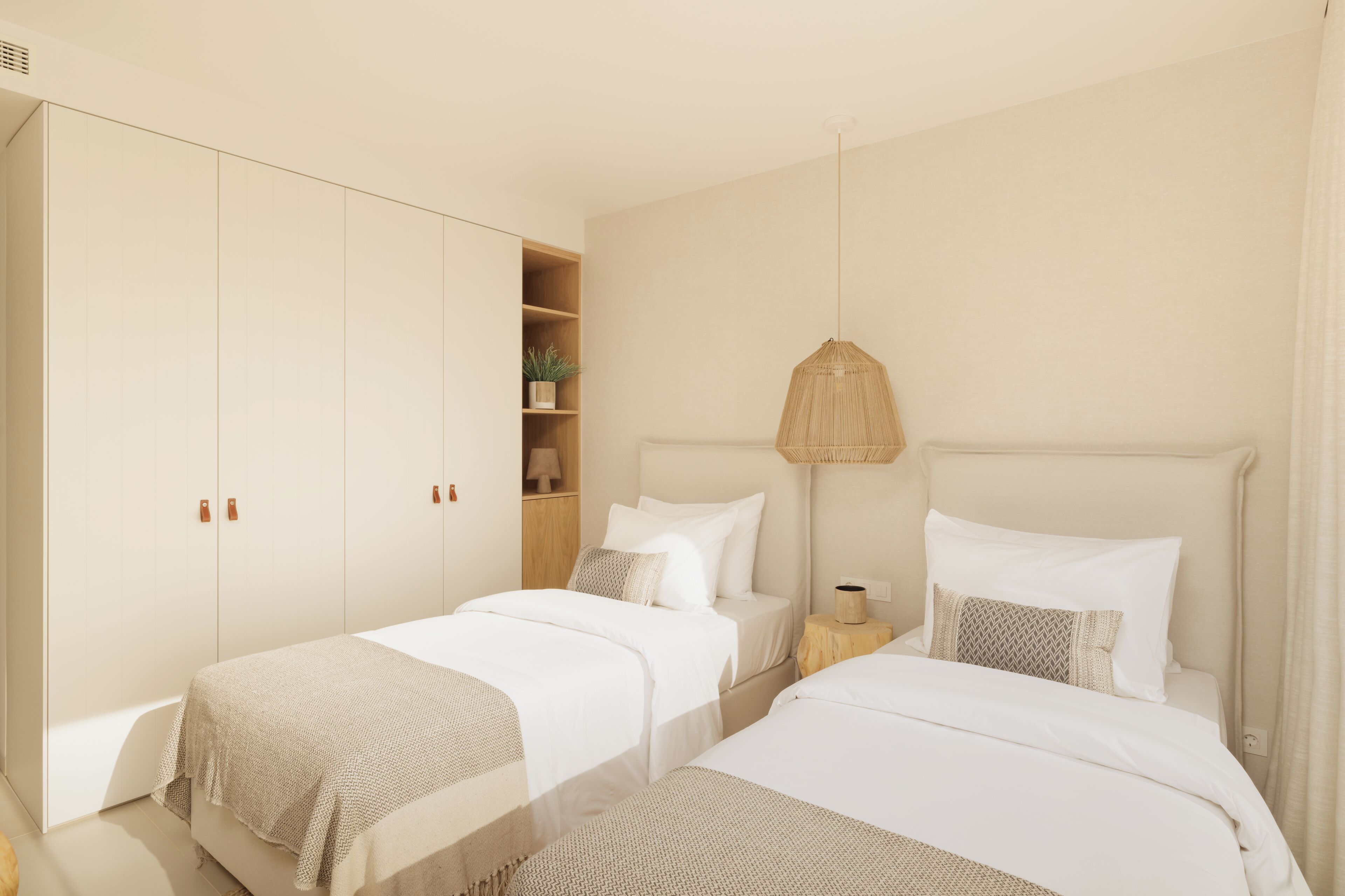 A bedroom with two beds, a wardrobe, a bedside table with a lamp, and a shelf with a plant.