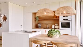 A modern kitchen with white cabinetry, a wooden dining table, two wicker pendant lights, and a built-in oven.