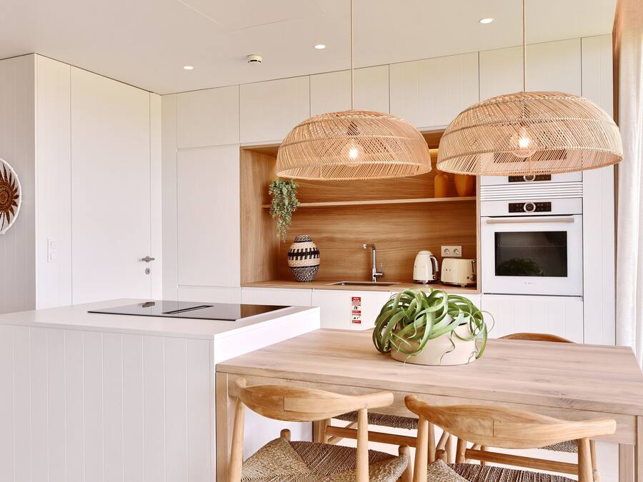 A modern kitchen with white cabinetry, a wooden dining table, two wicker pendant lights, and a built-in oven.