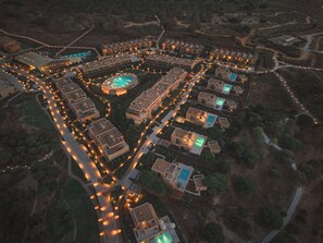 An aerial view of a resort with multiple buildings, swimming pools, and well-lit pathways.