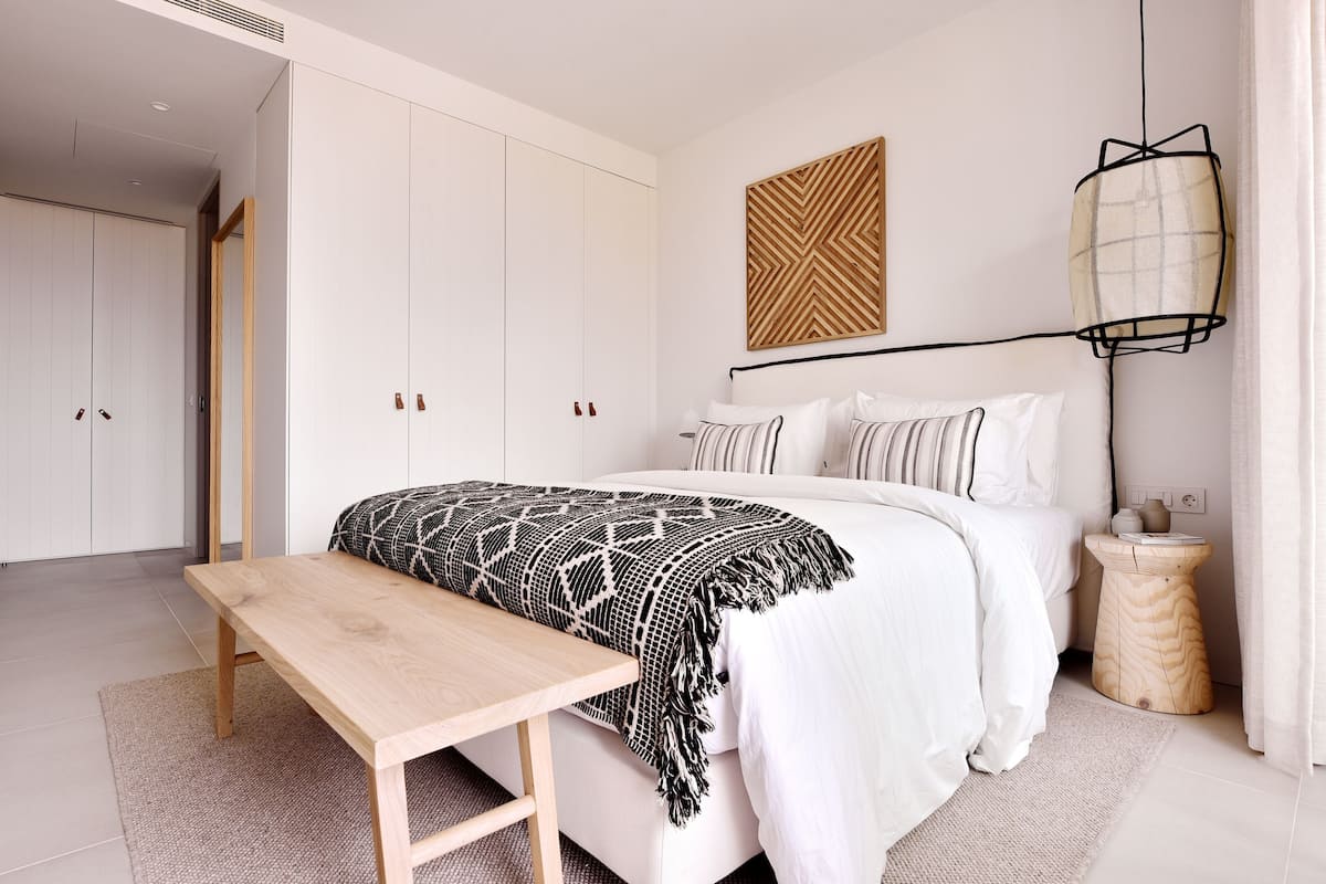 Un dormitorio moderno con una cama grande, un banco de madera, una mesita de noche y un aplique de pared.