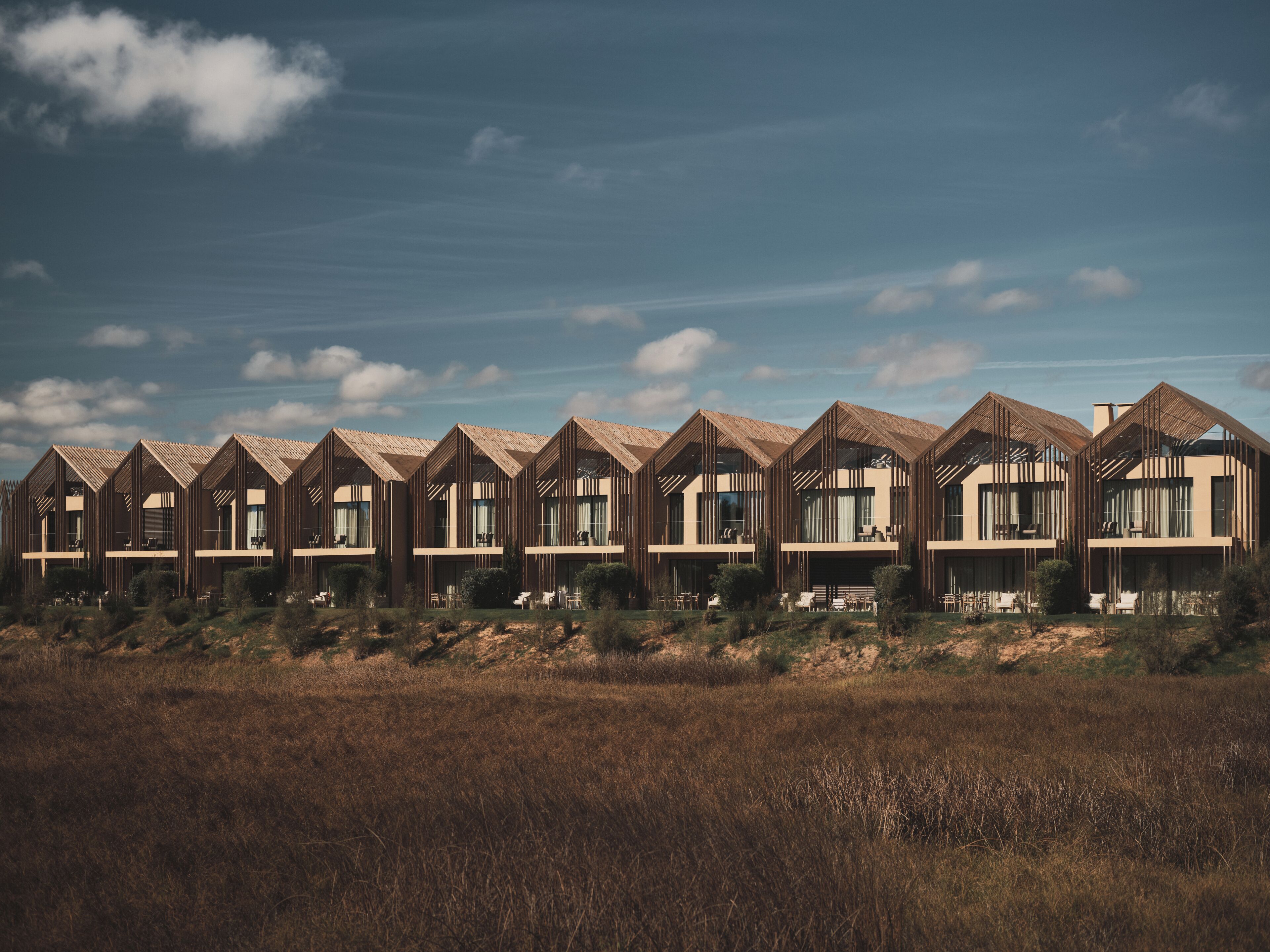 A row of modern, multi-story buildings with large windows and a flat roof, set in a grassy field with a clear sky.