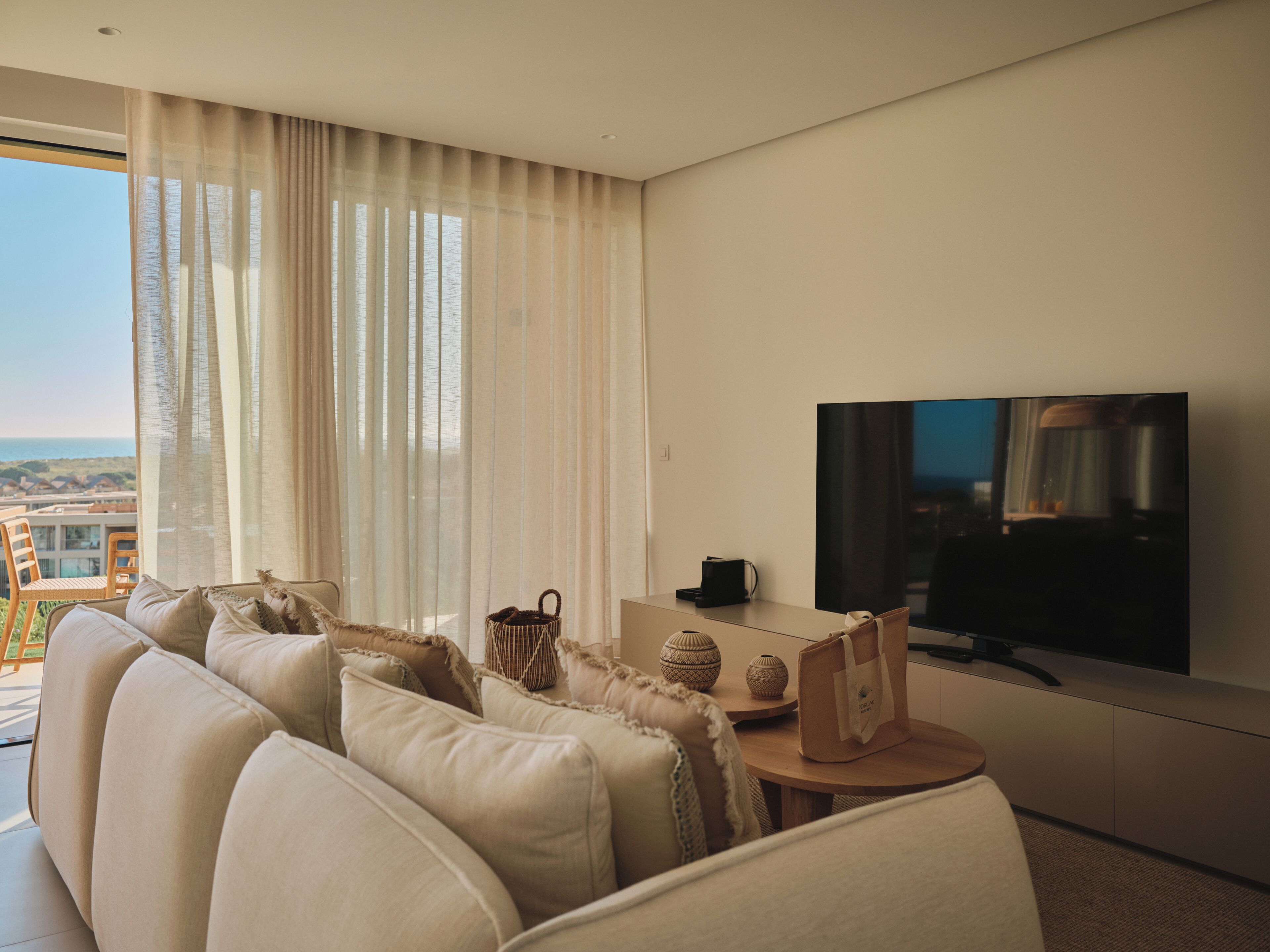 A modern living room with a sofa, television, and a view of the ocean.