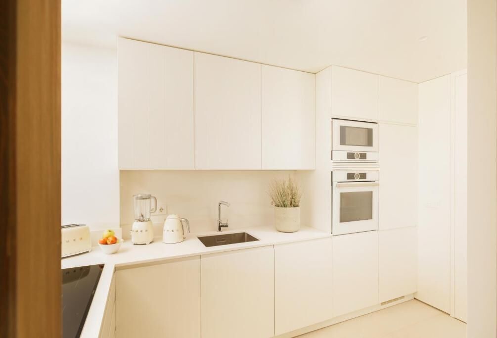 A modern kitchen with white cabinets, a built-in oven, a microwave, a sink, and a toaster.
