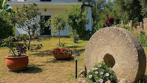 Uma casa de dois andares com varanda, cercada por um jardim com vasos de plantas e flores.