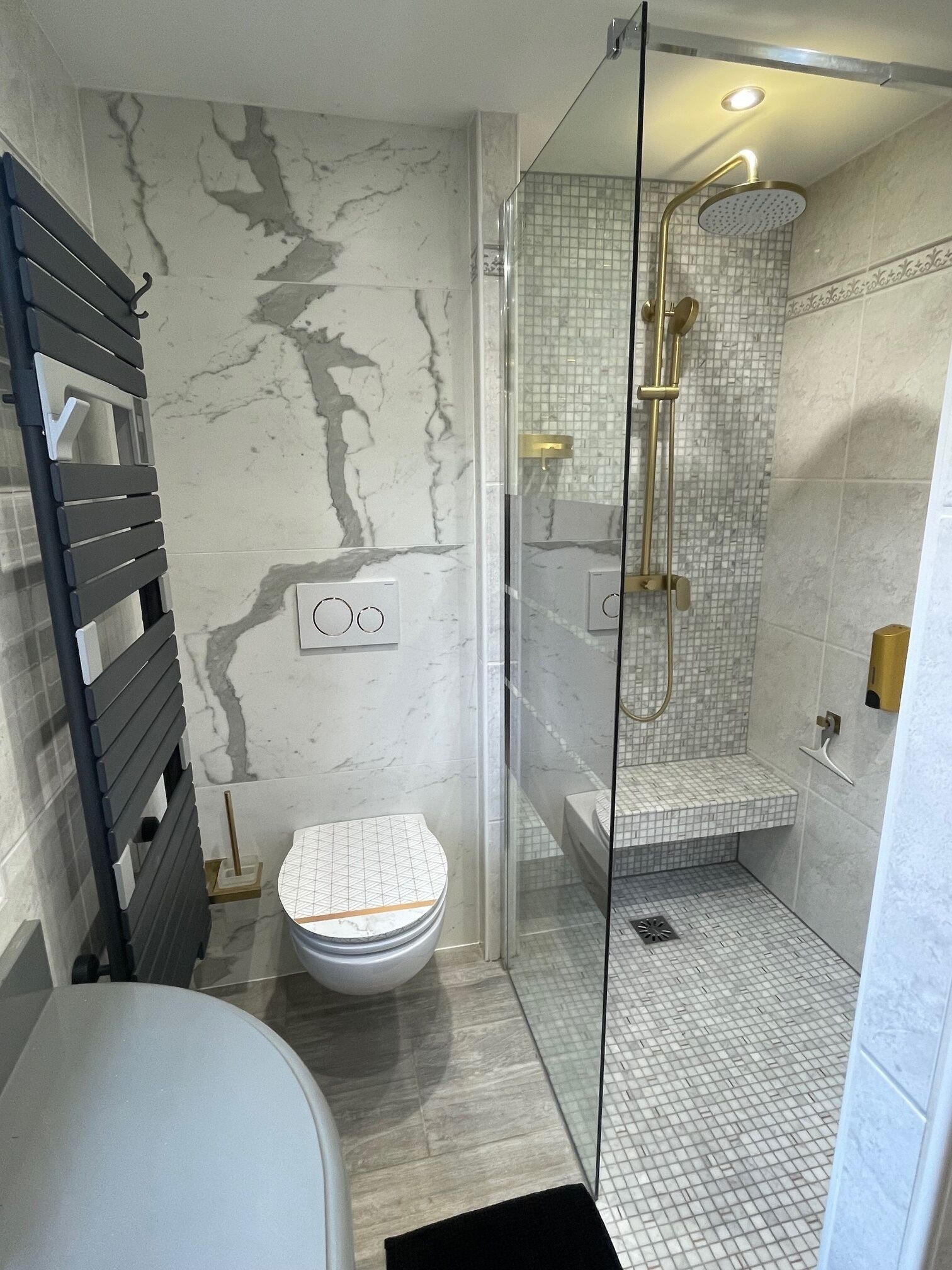 A bathroom with a marble wall, a glass-enclosed shower, and a toilet with a geometric pattern.