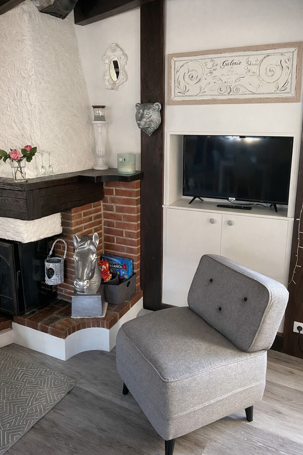 A living room with a fireplace, a television mounted on the wall, and a grey armchair.
