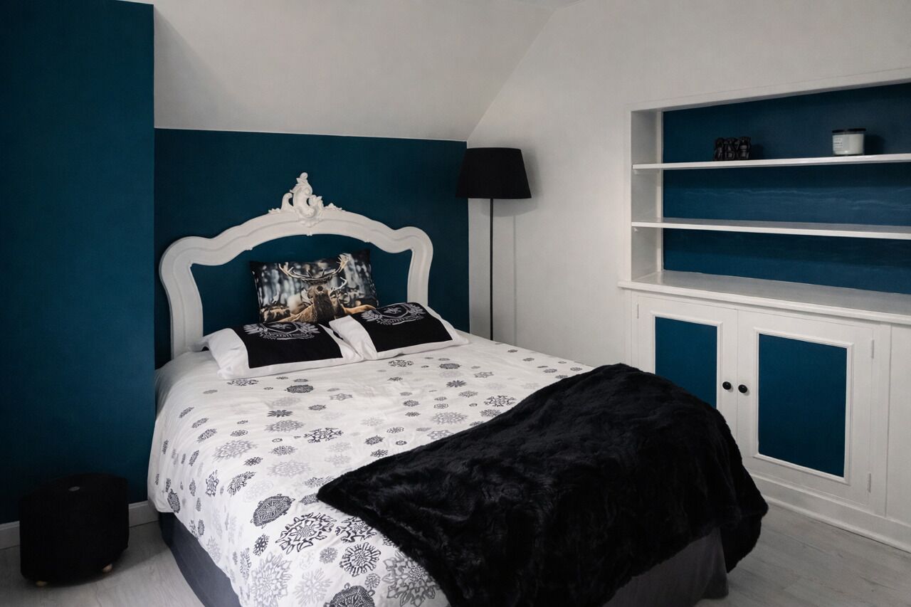 A bedroom with a bed, a black throw blanket, a white headboard, and a blue wall.