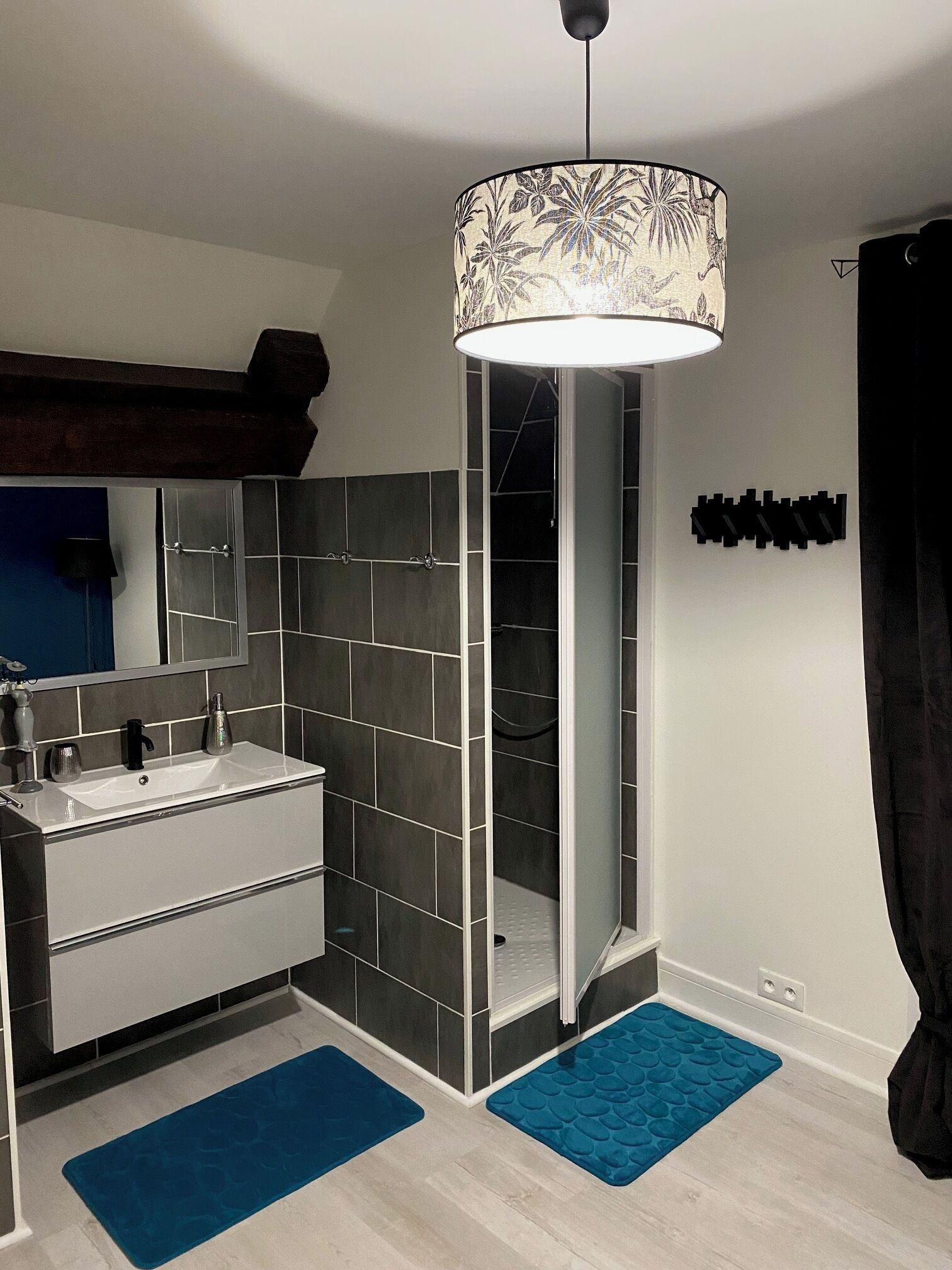 Een moderne badkamer met een wit wastafelmeubel, donker betegelde muren, een douche en een blauw vloerkleed.
