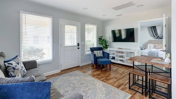 A living room with a sofa, armchair, coffee table, TV, and a dining area with a table and benches. - The Tea Olive Cottage, Quaint | Pet-Friendly! (Savannah)