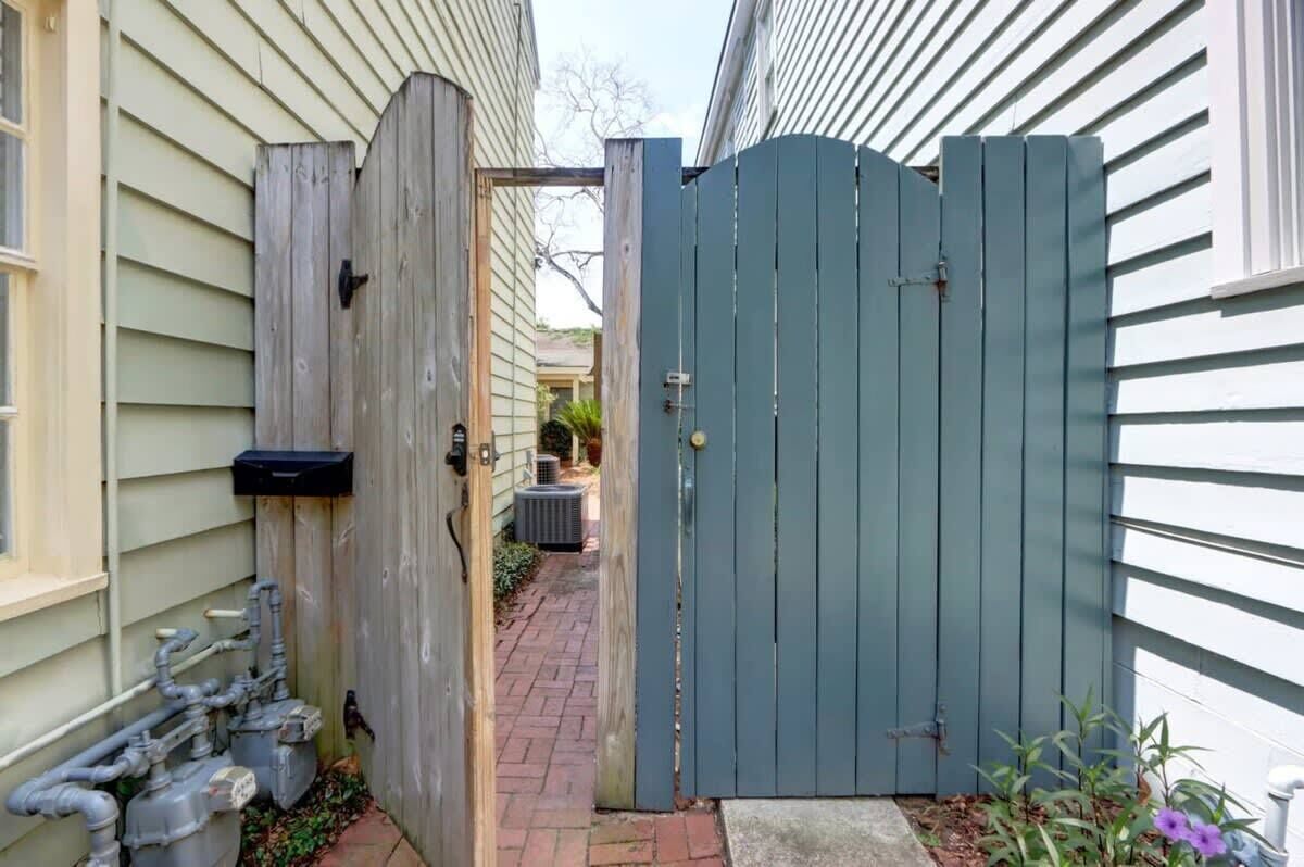 A gated entryway with a wooden gate, a brick pathway, and a small garden area with plants.