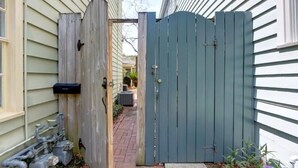 A gated entryway with a wooden gate, a brick pathway, and a small garden area with plants. - The Tea Olive Cottage, Quaint | Pet-Friendly! (Savannah)