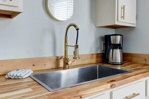 A kitchen with a stainless steel sink, a gold faucet, and a coffee maker on a wooden countertop. - The Tea Olive Cottage, Quaint | Pet-Friendly! (Savannah)