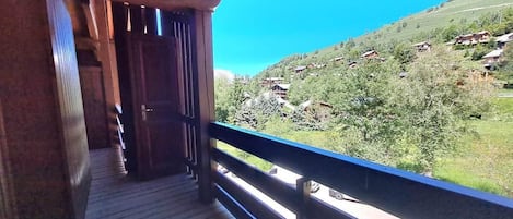 A wooden balcony with a view of a green valley and a clear blue sky.
