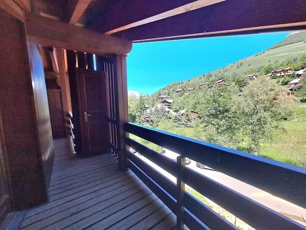 A wooden balcony with a view of a green valley and a clear blue sky.