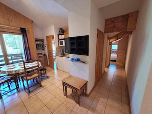 A spacious kitchen with a dining area, wooden beams, a flat-screen TV, and a view of the outdoors.