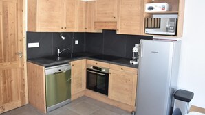 A compact kitchen with wooden cabinets, a dishwasher, an oven, a microwave, and a refrigerator. - 250m from ski slopes, Ground floor, terrace, parking, tv, ski locker, 47m², Pralognan-la-Vanoise (Pralognan-la-Vanoise)