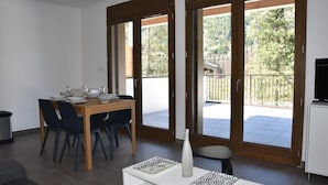 A dining area with a wooden table and chairs, a white cabinet, and a balcony with a view of greenery and a fence. - 250m from ski slopes, Ground floor, terrace, parking, tv, ski locker, 47m², Pralognan-la-Vanoise (Pralognan-la-Vanoise)
