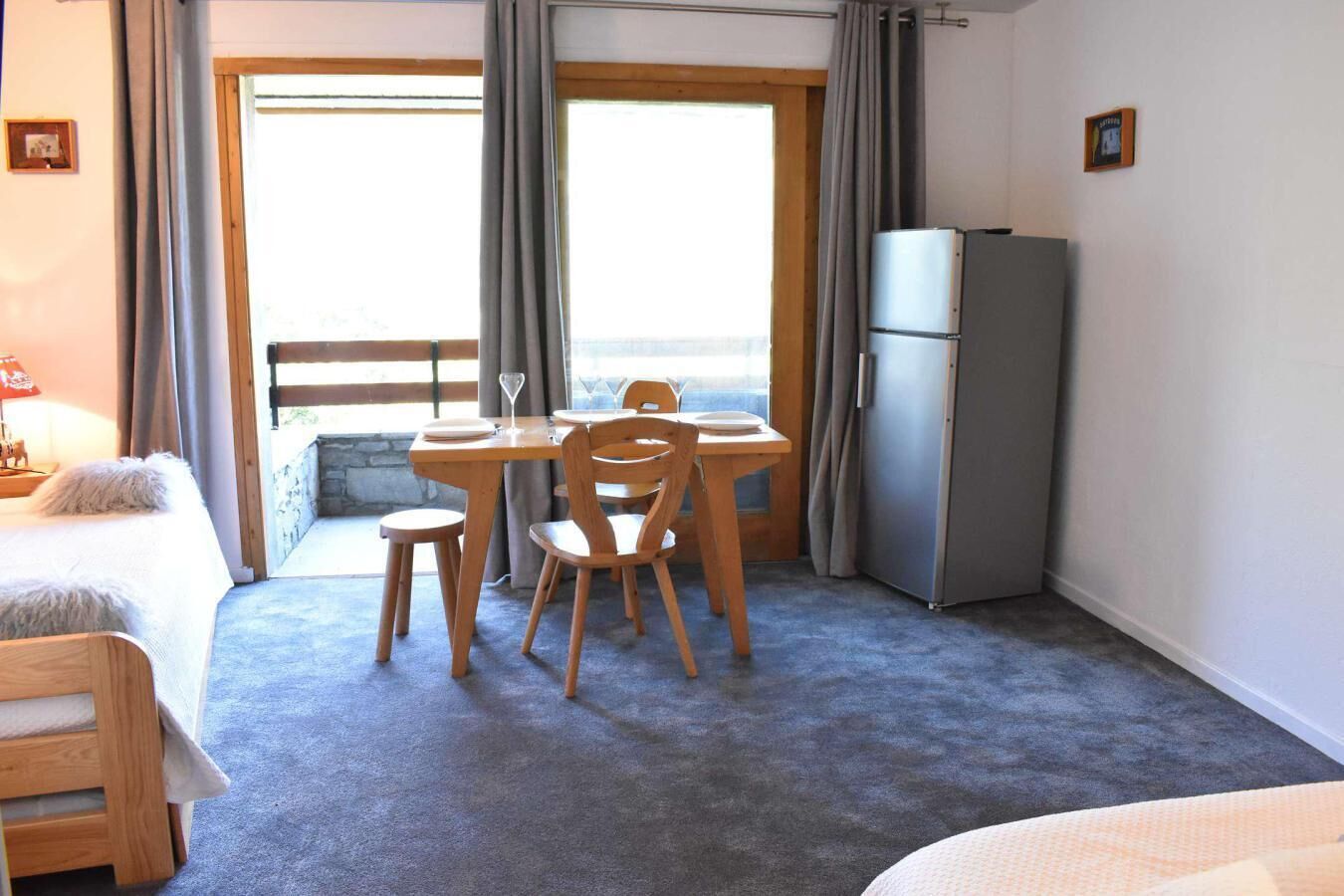 A room with a bed, a dining table with chairs, a refrigerator, and a view of the outdoors.