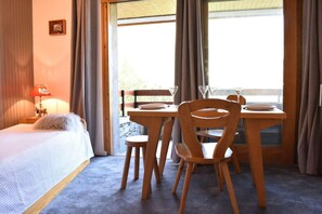 Une chambre d’hôtel avec un lit, une table en bois avec des chaises, une lampe rouge et une fenêtre avec des rideaux.