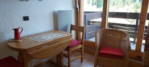 Una mesa de madera con un mantel individual, una silla de mimbre con un cojín rojo y una jarra roja sobre un posavasos.