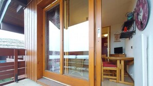 A wooden balcony with a sliding glass door leading to a room with a wooden table and a chair. - 3rd floor, view ski slopes, balcony, tv, ski locker, 13m², Valmorel (Valmorel)