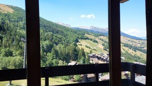 A view from a window overlooking a valley with a small village, surrounded by forested hills and mountains. - 3rd floor, view ski slopes, balcony, tv, ski locker, 13m², Valmorel (Valmorel)
