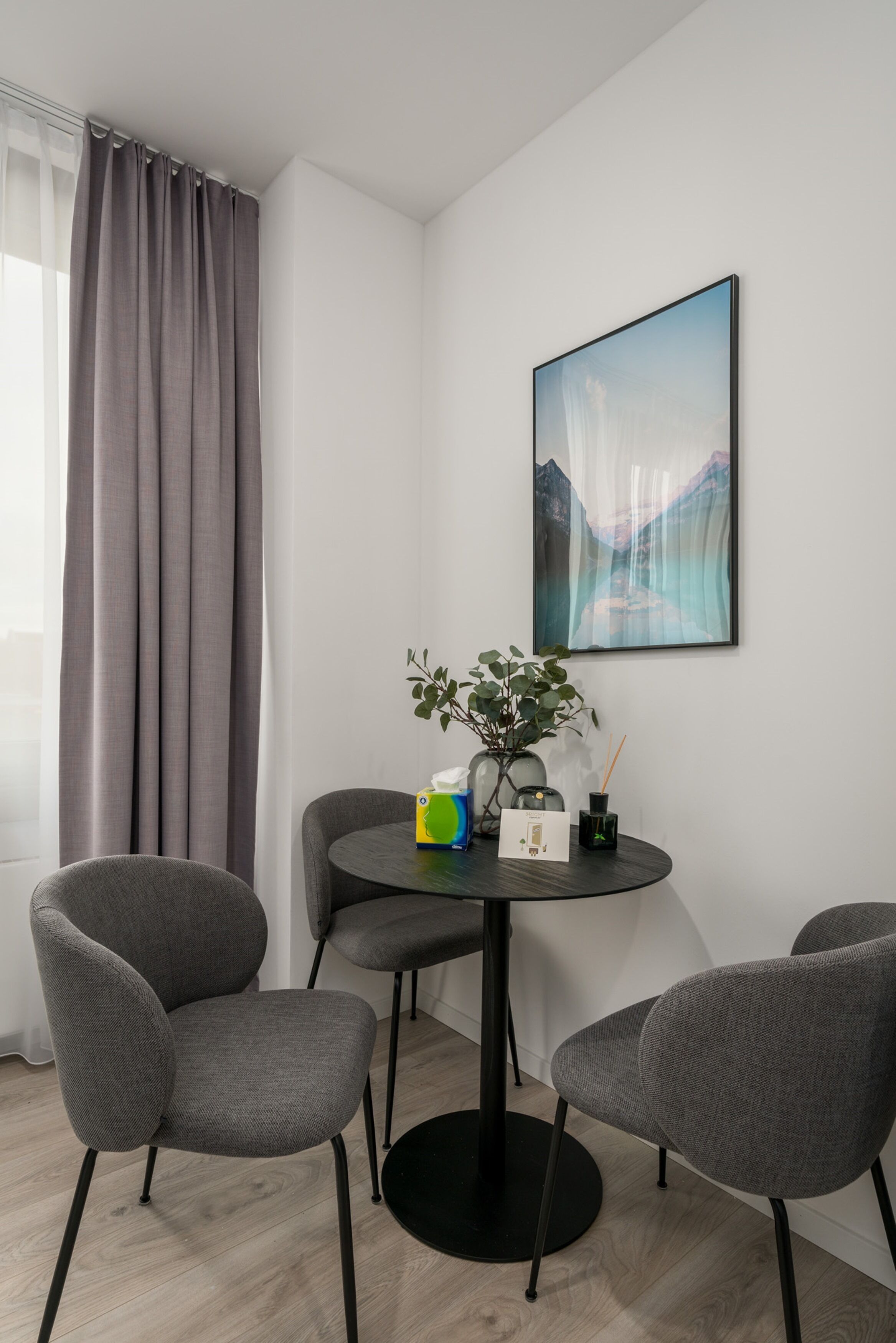 A modern room with a round table, two grey chairs, a potted plant, and a framed picture on the wall.