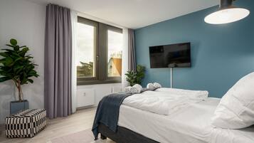Une chambre moderne avec un grand lit, un téléviseur fixé au mur et une fenêtre avec des rideaux.