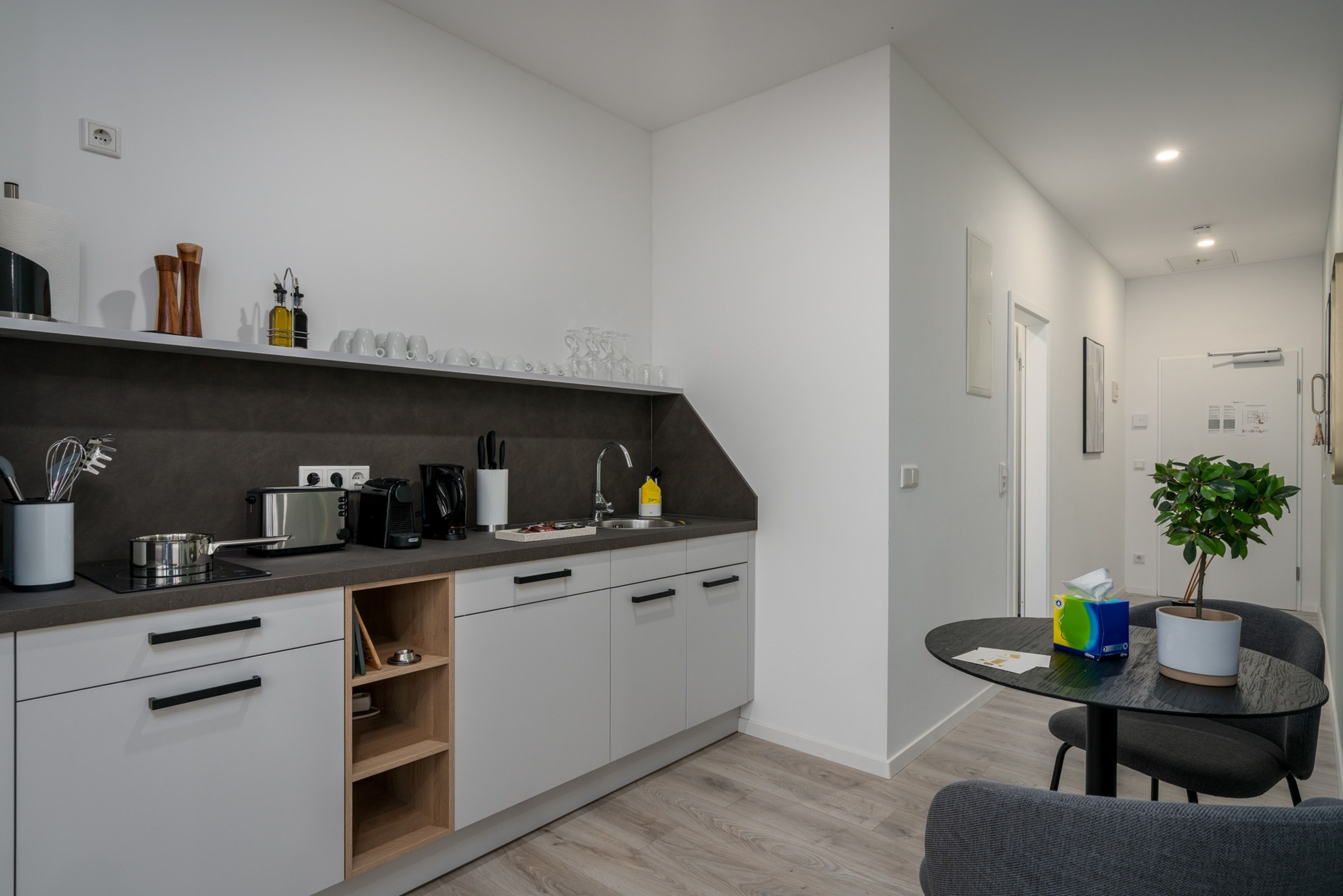 A modern kitchen with white cabinets, a dark countertop, and a dining area with a table and chairs.