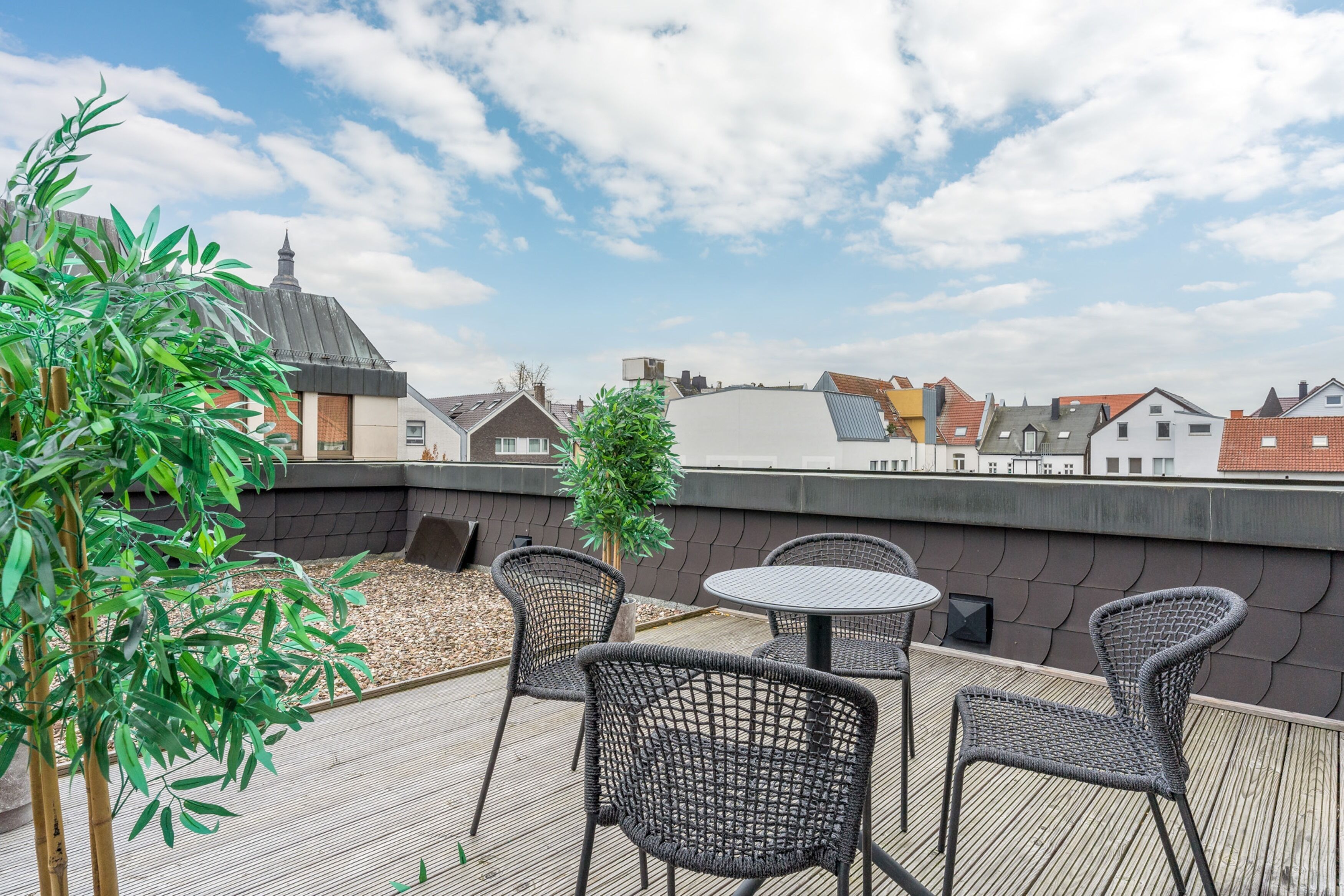 Terraço no terraço com cadeiras de vime e uma mesa, cercado por vegetação e com vista para a cidade.