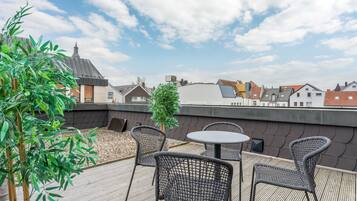 Terraço no terraço com cadeiras de vime e uma mesa, cercado por vegetação e com vista para a cidade.