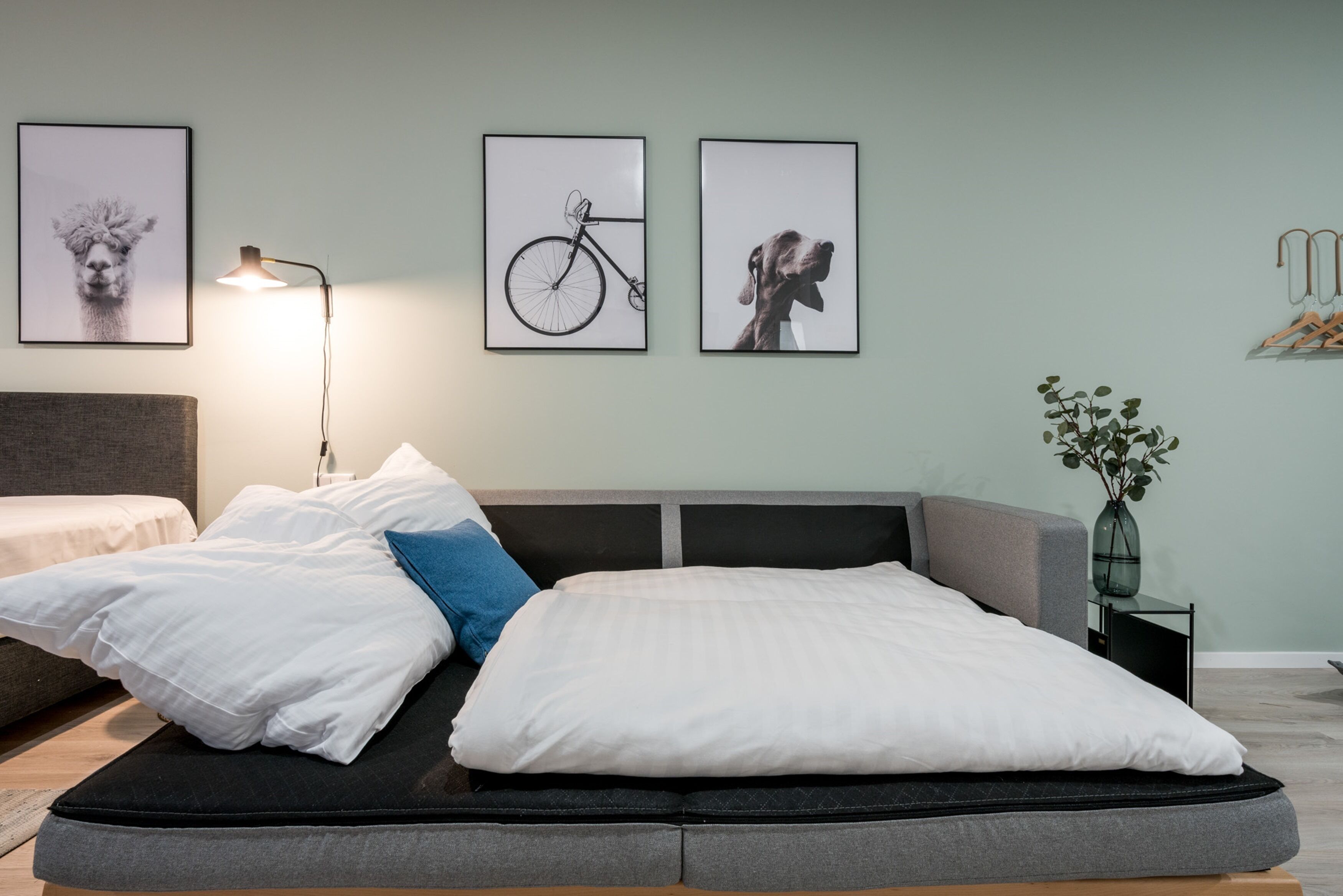 Quarto moderno com cama, mesa de cabeceira, abajur e quadros nas paredes.