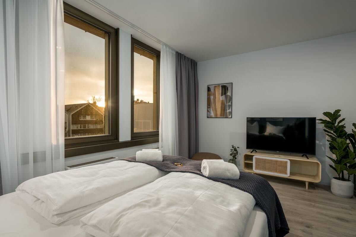 Een moderne hotelkamer met een groot bed, een televisie en uitzicht op de skyline.